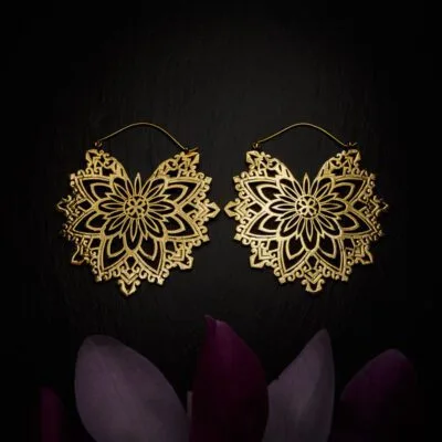 KIWA jewellery brand product image of a pair of brass large earrings called Abundance, set on a dark granite background with dark purple coloured flower decoration on the lower end.