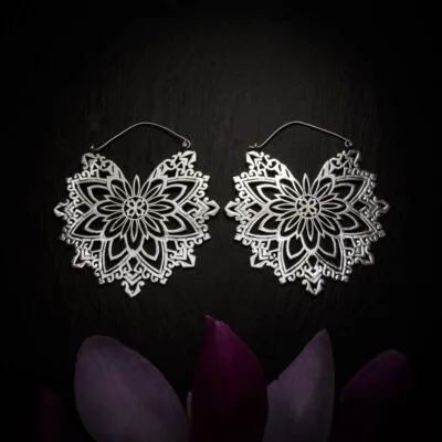 KIWA jewellery brand product image of a pair of silver plated large earrings called Abundance, set on a dark granite background with dark purple coloured flower decoration on the lower end.