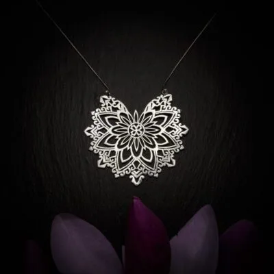 KIWA jewellery brand product image of a large silver plated pendant necklace called Abundance. The necklace is set on a dark granite background with purple colored flower decoration on the lower end