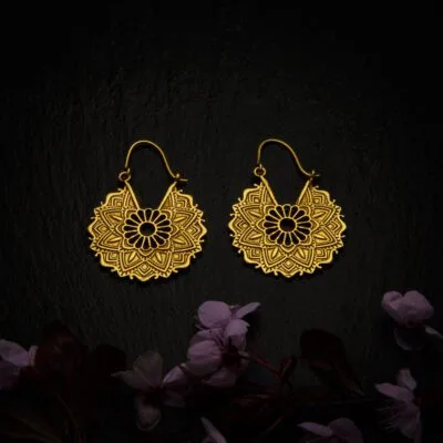 KIWA jewellery brand product image of a pair of brass material earrings called Bali, set on a dark granite background with dark pink coloured flower decoration on the lower end.