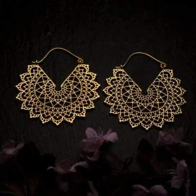 KIWA jewellery brand product image of a pair of brass material earrings called Basilicum, set on a dark granite background with dark pink coloured flower decoration on the lower end.