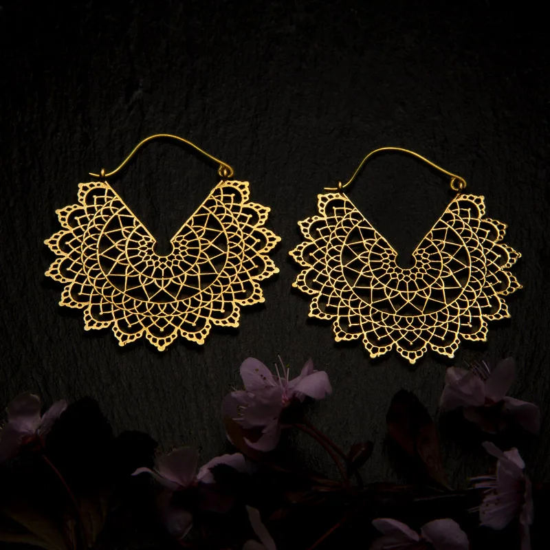 KIWA jewellery brand product image of a pair of brass material earrings called Basilicum, set on a dark granite background with dark pink coloured flower decoration on the lower end.