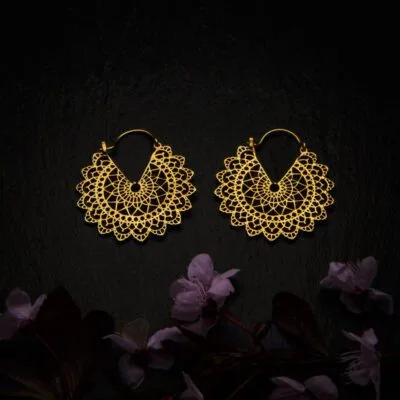KIWA jewellery brand product image of a pair of brass material earrings called Basilicum mini version, set on a dark granite background with dark pink coloured flower decoration on the lower end.