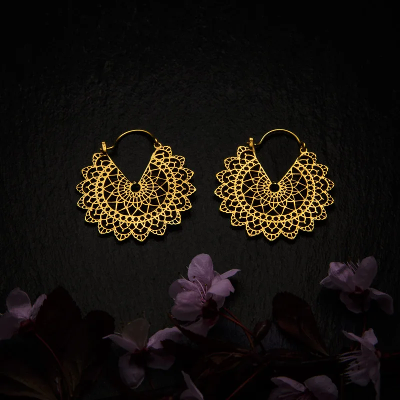 KIWA jewellery brand product image of a pair of brass material earrings called Basilicum mini version, set on a dark granite background with dark pink coloured flower decoration on the lower end.