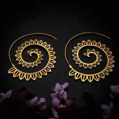 KIWA jewellery brand product image of a pair of brass material earrings called Big Spirals, set on a dark granite background with dark pink coloured flower decoration on the lower end.