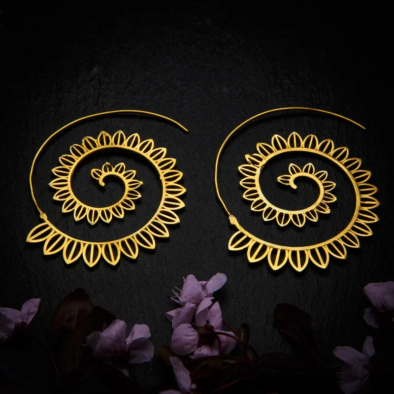 KIWA jewellery brand product image of a pair of brass material earrings called Big Spirals, set on a dark granite background with dark pink coloured flower decoration on the lower end.