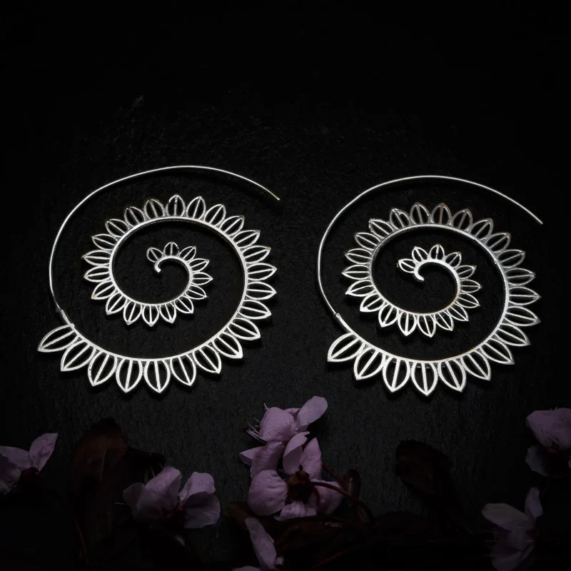 KIWA jewellery brand product image of a pair of silver plated earrings called Big spirals , set on a dark granite background with dark pink coloured flower decoration on the lower end.