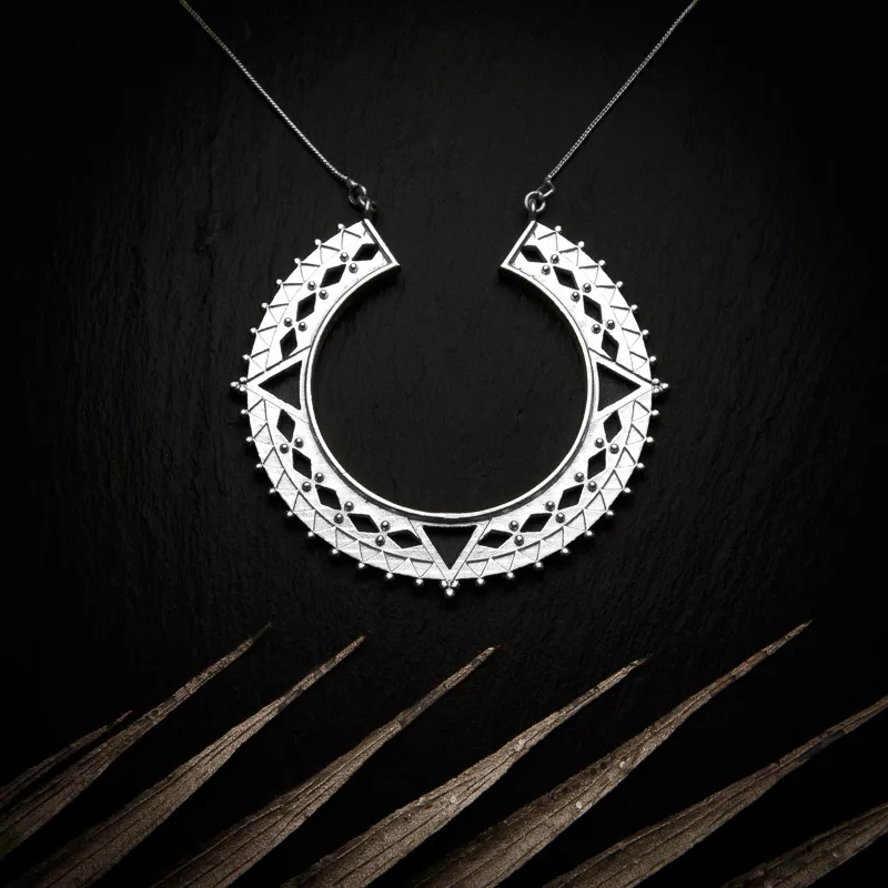 KIWA jewellery brand product image of a star model silver plated pendant necklace called Bozo. The necklace is set on a dark granite background with light colored leaf decoration on the lower end