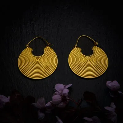 KIWA jewellery brand product image of a pair of brass material earrings called Cycle, set on a dark granite background with dark pink coloured flower decoration on the lower end.