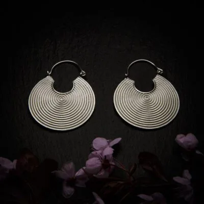 KIWA jewellery brand product image of a pair of silver plated earrings Cycle , set on a dark granite background with dark pink coloured flower decoration on the lower end.