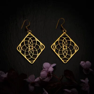 KIWA jewellery brand product image of a pair of brass material earrings called Experience, set on a dark granite background with dark pink coloured flower decoration on the lower end.