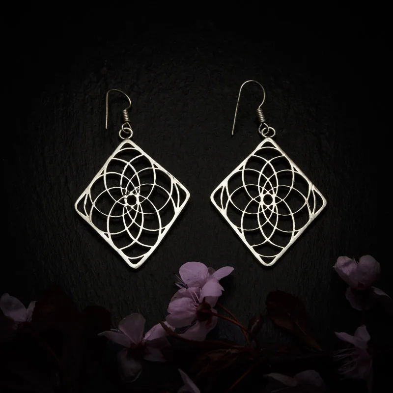 KIWA jewellery brand product image of a pair of silver plated earrings called Experience, set on a dark granite background with dark pink coloured flower decoration on the lower end.