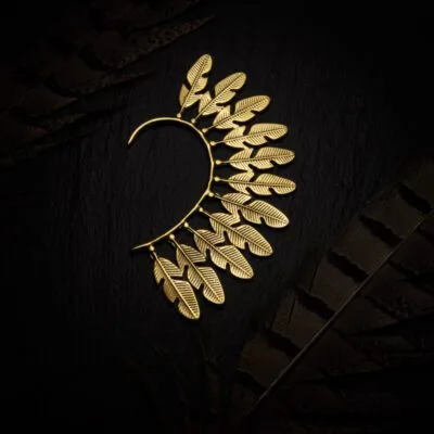 KIWA jewellery brand product image of a single brass material earring called the Feather earcuff. The earcuff is set on a dark granite background with feather decoration