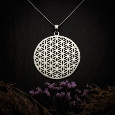 KIWA jewellery brand product image of a silver plated pendant necklace called Flower of Life. The necklace is set on a dark granite background with hay and dark purple flower decoration on the lower end