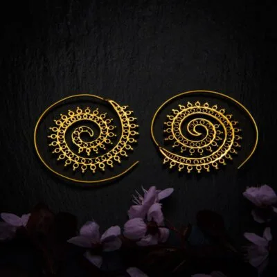 KIWA jewellery brand product image of a pair of brass material earrings called Funky Spirals, set on a dark granite background with dark pink coloured flower decoration on the lower end.