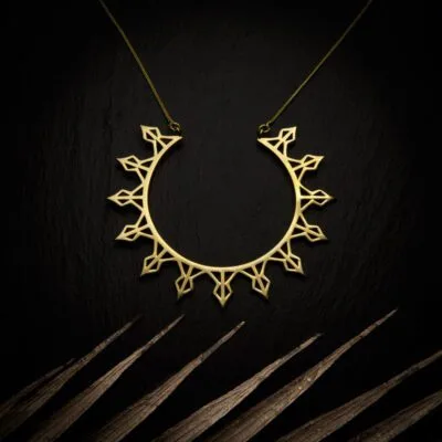 KIWA jewellery brand product image of a brass material pendant necklace called Helia. The necklace is set on a dark granite background with light colored leaf decoration on the lower end