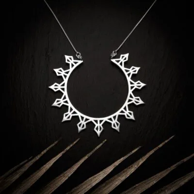 KIWA jewellery brand product image of a silver plated pendant necklace called Helia. The necklace is set on a dark granite background with light colored leaf decoration on the lower end