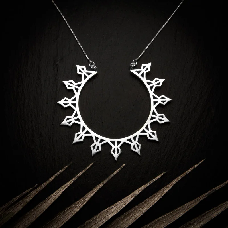 KIWA jewellery brand product image of a silver plated pendant necklace called Helia. The necklace is set on a dark granite background with light colored leaf decoration on the lower end
