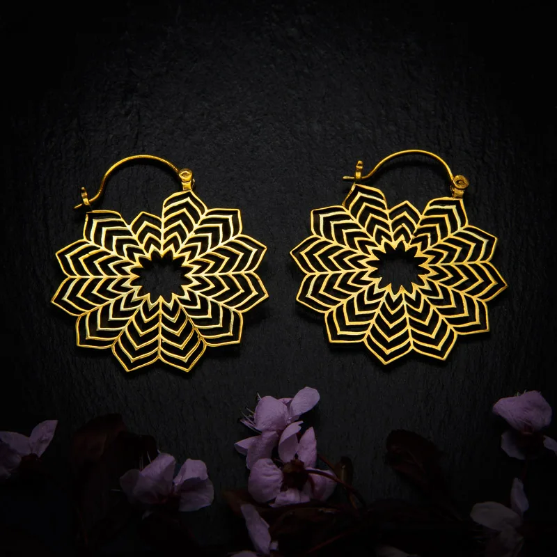 KIWA jewellery brand product image of a pair of brass material earrings called Hora, set on a dark granite background with dark pink coloured flower decoration on the lower end.