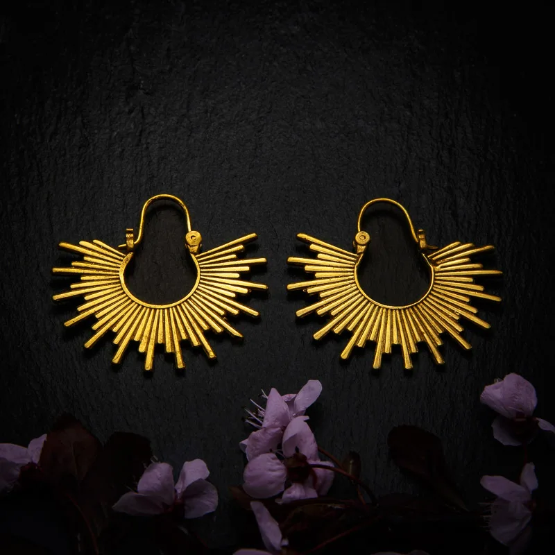 KIWA jewellery brand product image of a pair of brass material earrings called Island, set on a dark granite background with dark pink coloured flower decoration on the lower end.