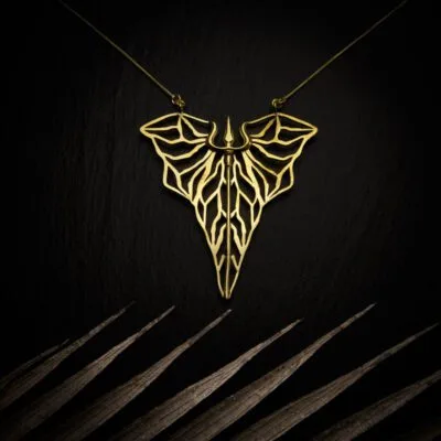KIWA jewellery brand product image of a brass material pendant necklace called Kali. The necklace is set on a dark granite background with light colored leaf decoration on the lower end