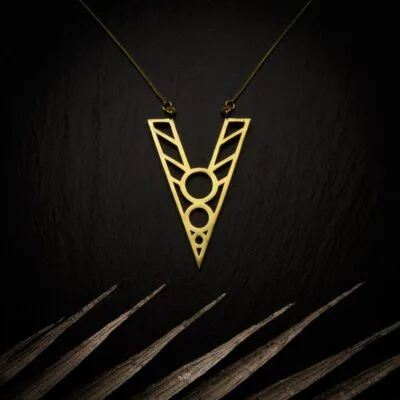 KIWA jewellery brand product image of a brass material pendant necklace called Kentaura. The necklace is set on a dark granite background with light colored leaf decoration on the lower end