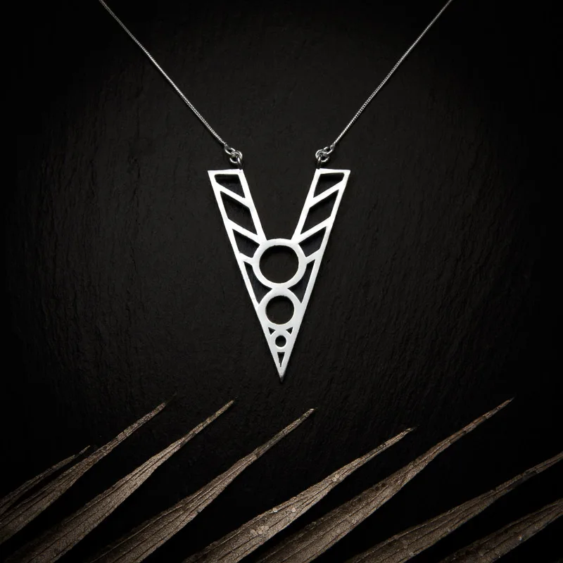 KIWA jewellery brand product image of a silver plated pendant necklace called Kentaura. The necklace is set on a dark granite background with light colored leaf decoration on the lower end
