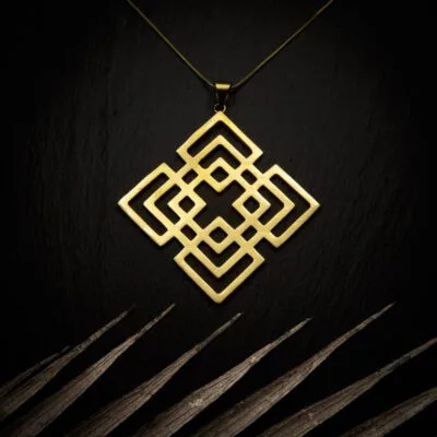 KIWA jewellery brand product image of a brass material pendant necklace called Mokosha. The necklace is set on a dark granite background with light colored leaf decoration on the lower end