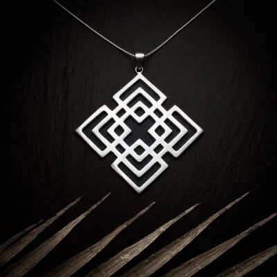 KIWA jewellery brand product image of a silver plated pendant necklace called Mokosha. The necklace is set on a dark granite background with light colored leaf decoration on the lower end