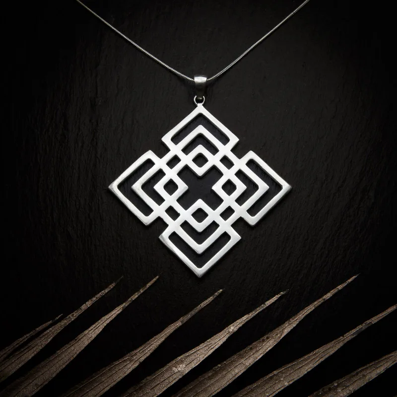 KIWA jewellery brand product image of a silver plated pendant necklace called Mokosha. The necklace is set on a dark granite background with light colored leaf decoration on the lower end