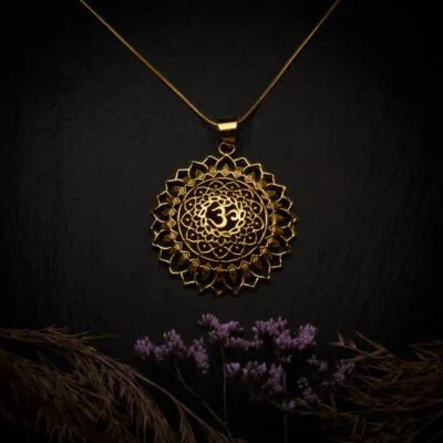 KIWA jewellery brand product image of a single brass material necklace called Om Sum, set on a dark granite background with hay and dark purpe flower decoration on the lower end