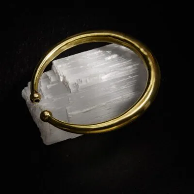 KIWA jewellery brand product image of a single brass armlet called the plain armlet. The armlet is set on a dark granite background on a selenite stone