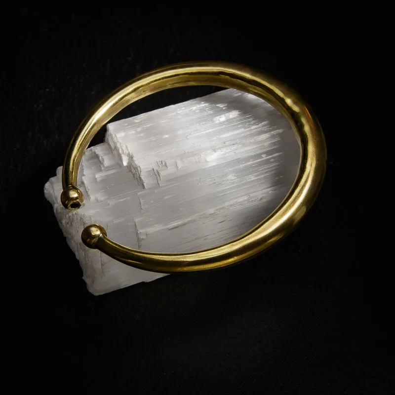 KIWA jewellery brand product image of a single brass armlet called the plain armlet. The armlet is set on a dark granite background on a selenite stone