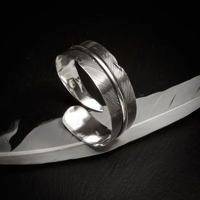 KIWA jewellery brand product image of a single silver plated armlet called the Queen armlet. The armlet is set on a dark granite background with white feather decoration