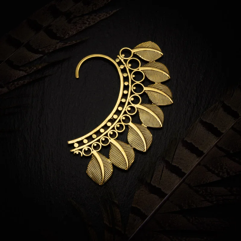 KIWA jewellery brand product image of a single brass material earring called the Serenity earcuff. The earcuff is set on a dark granite background with feather decoration