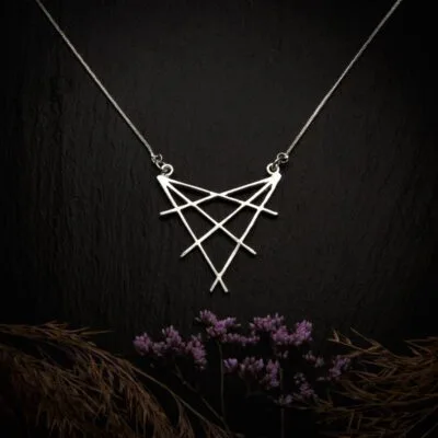 KIWA jewellery brand product image of a silver plated pendant necklace called Shibuya. The necklace is set on a dark granite background with hay and dark purple flower decoration on the lower end