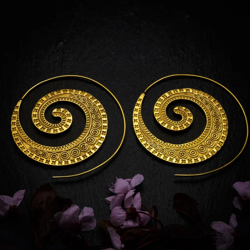KIWA jewellery brand product image of a pair of brass material earrings called the Spicy Spirals, set on a dark granite background with dark pink coloured flower decoration on the lower end.