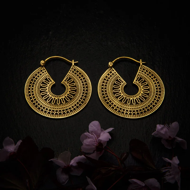 KIWA jewellery brand product image of a pair of brass material earrings called Taksim, set on a dark granite background with dark pink coloured flower decoration on the lower end.