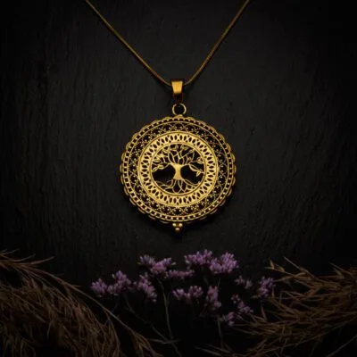 KIWA jewellery brand product image of a single brass material necklace called the Tree of Life, set on a dark granite background with hay and dark purpe flower decoration on the lower end