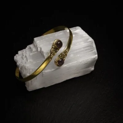 KIWA jewellery brand product image of a single brass armlet called the Two stone armlet. The armlet has a labradorite stone, but it comes in varieties. The armlet is set on a dark granite background on a selenite stone