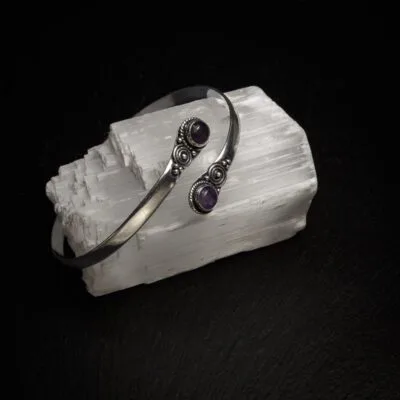 KIWA jewellery brand product image of a single silver plated armlet called the Two stone armlet. The armlet has a amethyst stone, but it comes in varieties. The armlet is set on a dark granite background on a selenite stone