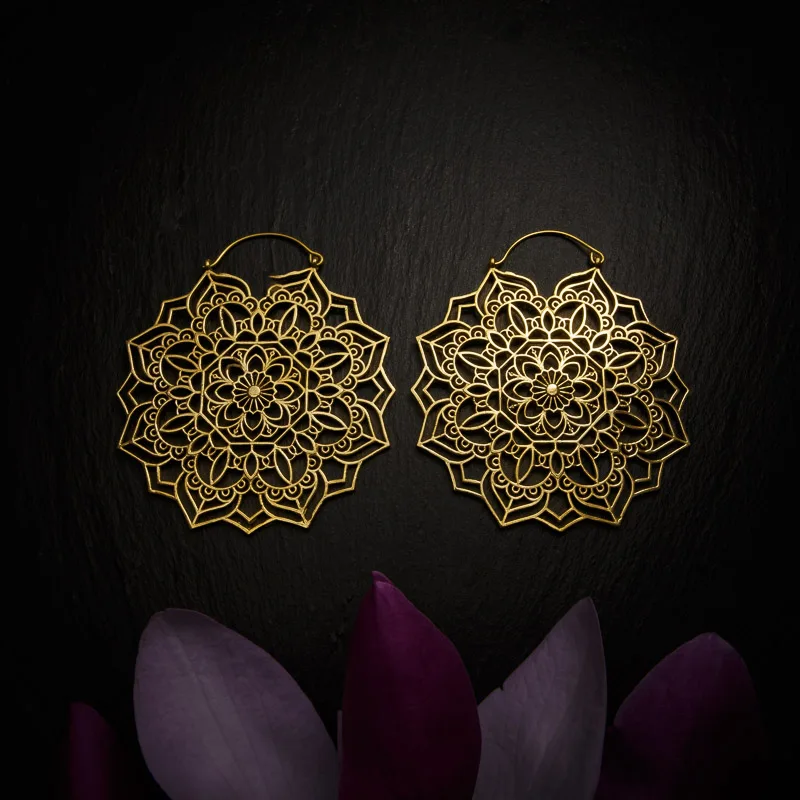 KIWA jewellery brand product image of a pair of large brass material earrings called Veda, set on a dark granite background with dark purple coloured flower decoration on the lower end.