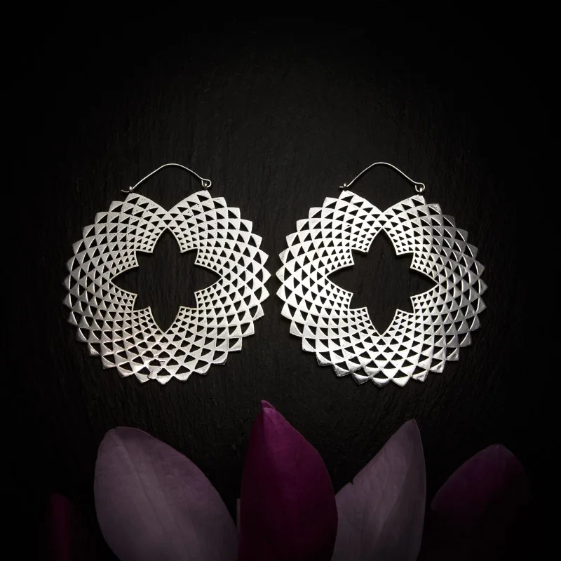 KIWA jewellery brand product image of a pair of silver plated large earrings called Vega, set on a dark granite background with dark purple coloured flower decoration on the lower end.