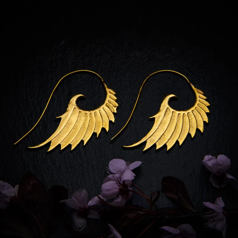KIWA jewellery brand product image of a pair of brass material earrings called Wing, set on a dark granite background with dark pink coloured flower decoration on the lower end.
