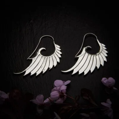 KIWA jewellery brand product image of a pair of silver plated earrings called Wing, set on a dark granite background with dark pink coloured flower decoration on the lower end.
