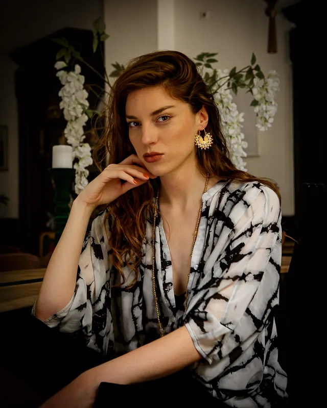 Photo of a Female model wearing Emilia Earrings Brass from KIWA jewelry in a Boho style apartment with a black and white shirt