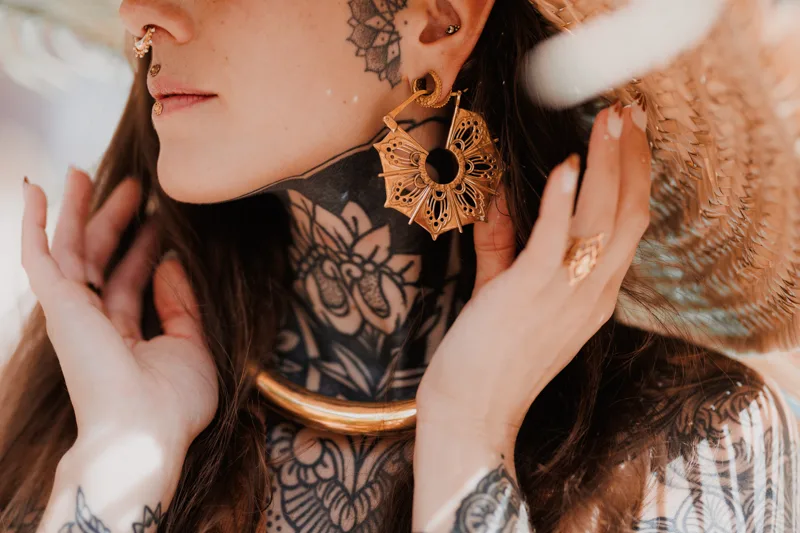 Photo of a Female model wearing Gaia Brass Earrings from KIWA Jewellery handcrafted designs wearing a huge straw hat. The model is rich in body art