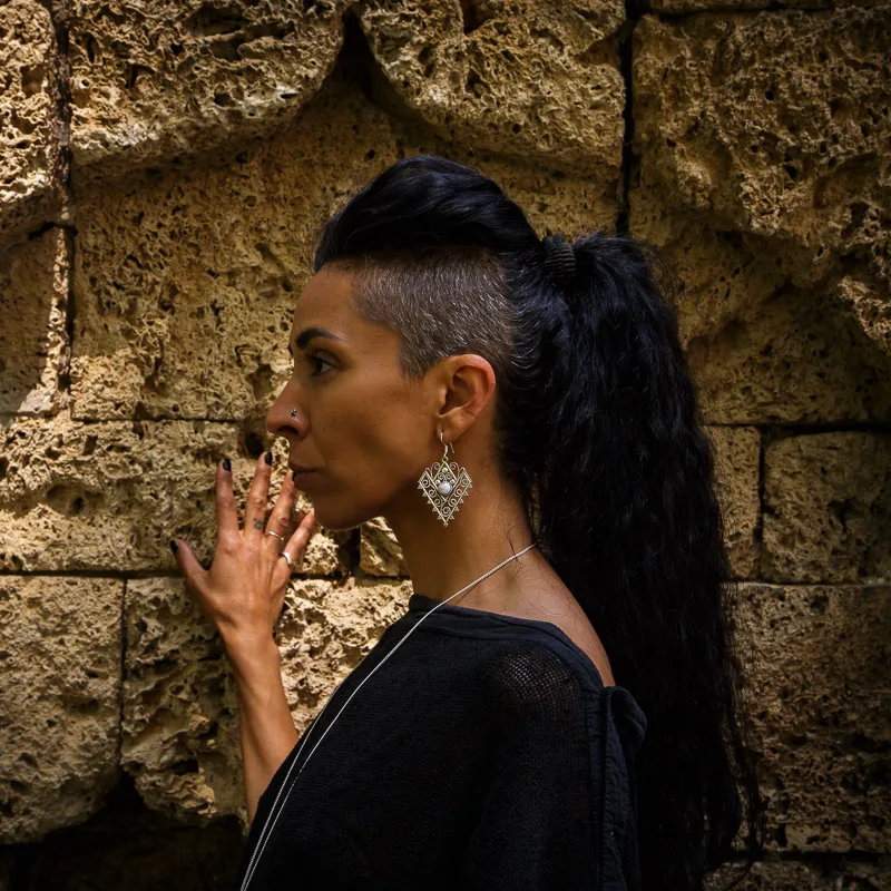 Photo of a Female model wearing Love Earrings Silver plated from KIWA jewellery against a turkish sand stone hamam