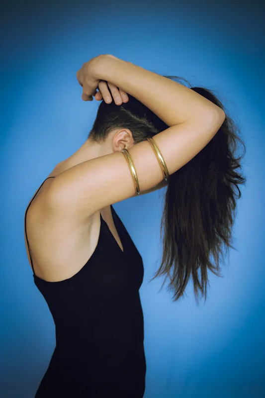 Photo of a Female model wearing Plain Armlet Brass from KIWA Jewellery set against a blue background