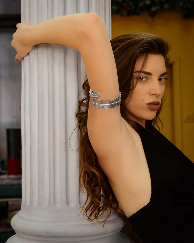 Photo of a Female model wearing Queen Armlet Silver Plated from KIWA Jewellery while leaning against a white pillar in a bohemian aparment while wearing a black dress
